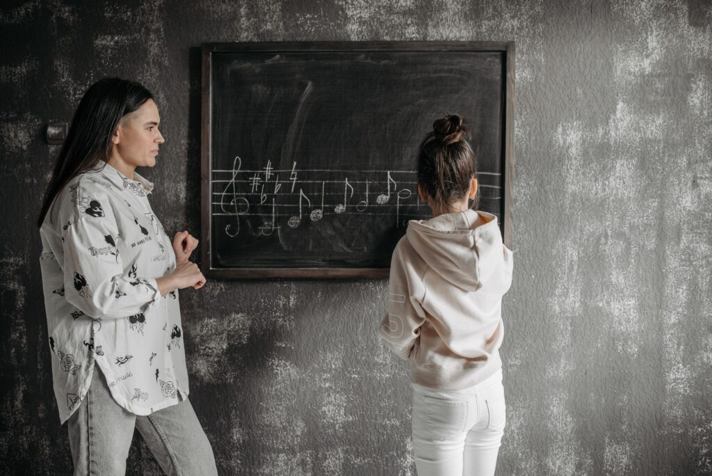 A mother instructs her daughter in music notation at a blackboard, fostering learning.