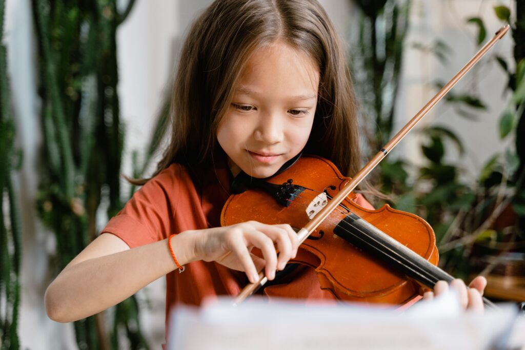 A young girl playing the violin with concentration in an indoor setting.