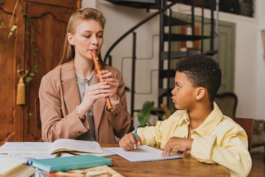 Boy learning flute with teacher during music lesson indoors.